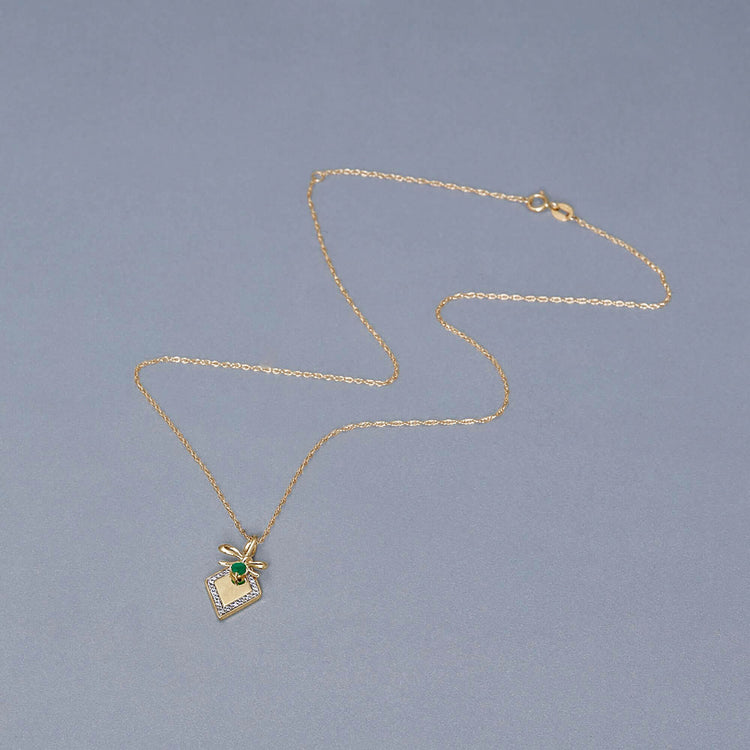 Stone and Strand 10K Yellow Gold Bow Nouveau Diamond and Emerald Tag Necklace Editorial Image